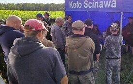 przed niebieskim namiotem stoi grupa mężczyzna odwr&oacute;cona tyłem na obrazku