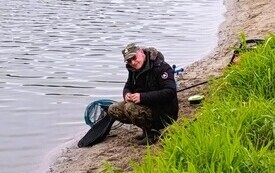 nad brzegiem wody kuca mężczyzna w czapce i nawleka na haczyk robaka, będzie wędkował