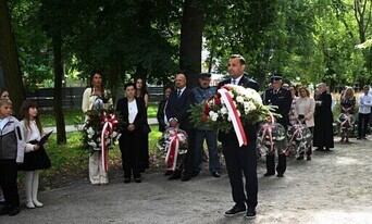 w parku grupa osób stojąca i patrząca na meżczyznę składającego kwiaty