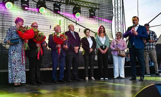 grupa ludzi stojacych na scenie, trzy osoby trzymaja kwiaty w rękach